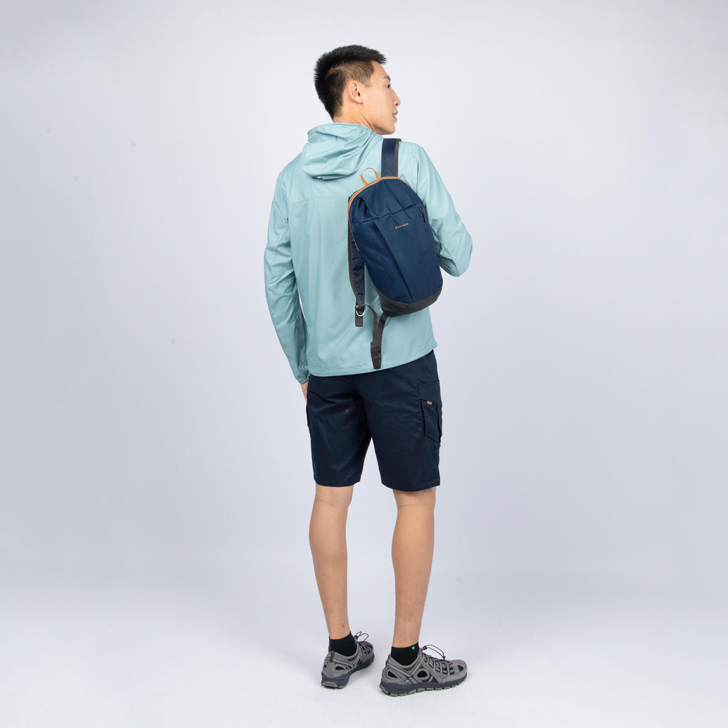Person wearing a light blue jacket and dark shorts with a navy backpack on a white background