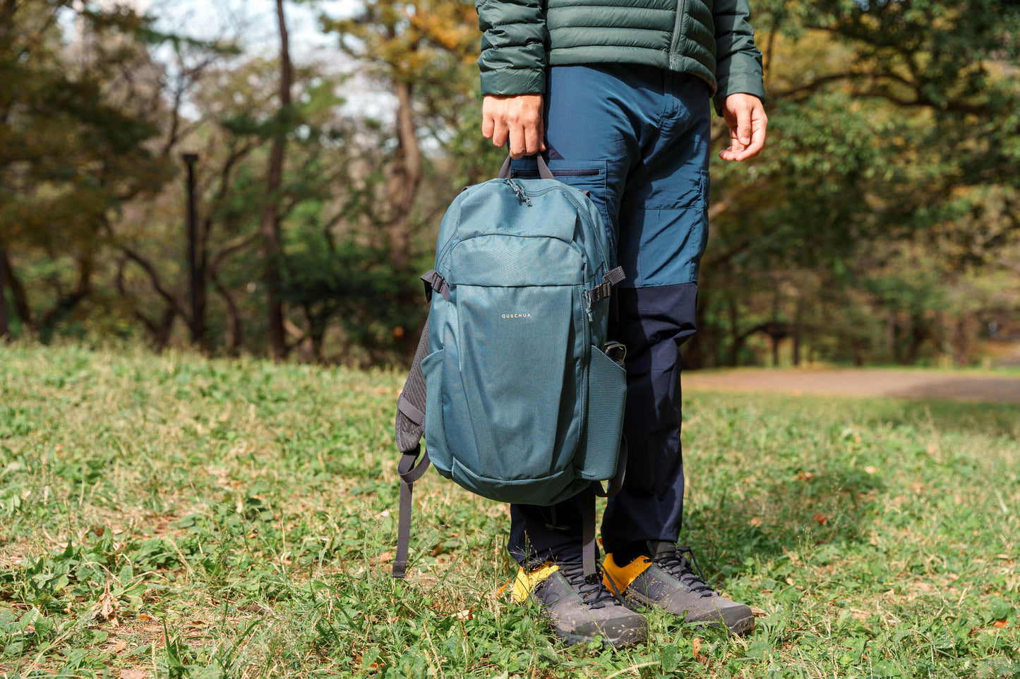 Person holding a teal backpack in a grassy outdoor setting