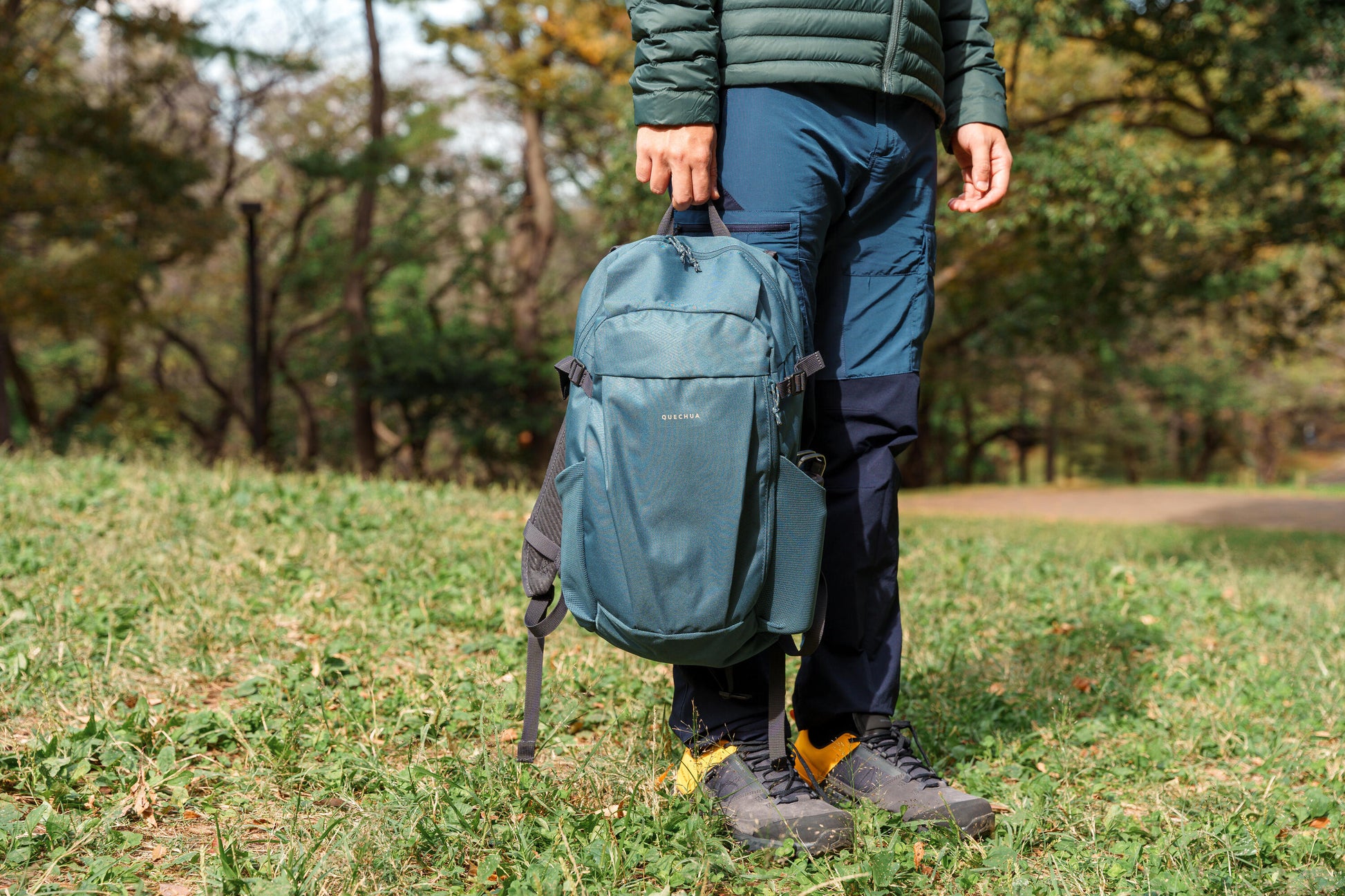 Person holding a teal backpack in a grassy outdoor setting