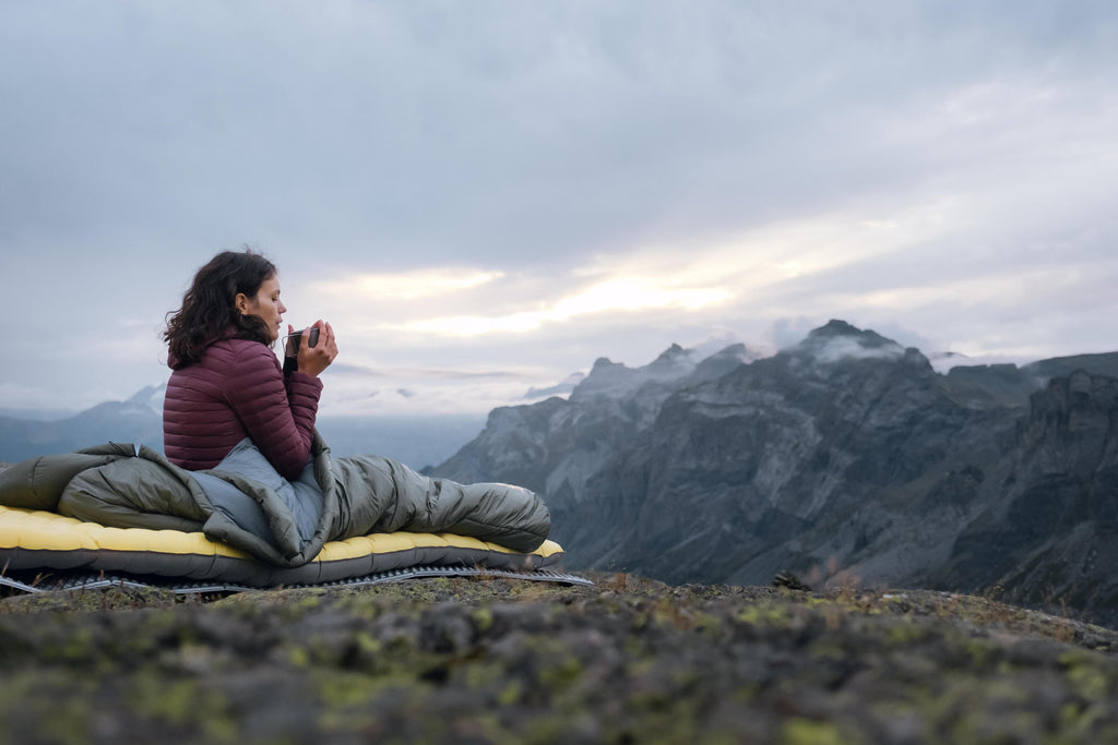Person sitting on a sleeping bag with mountains in the background