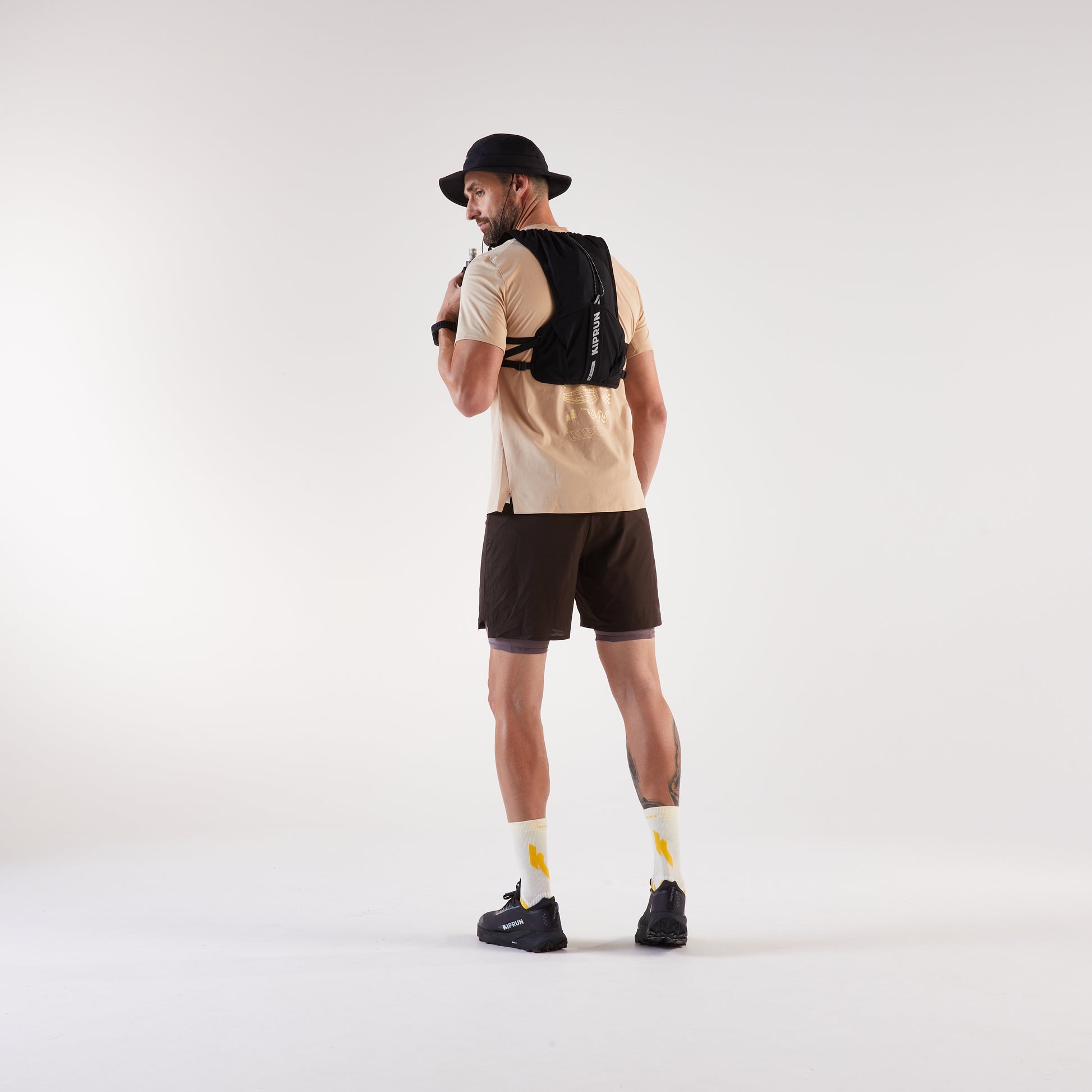 Man wearing a beige shirt, black shorts, and a black backpack on a white background