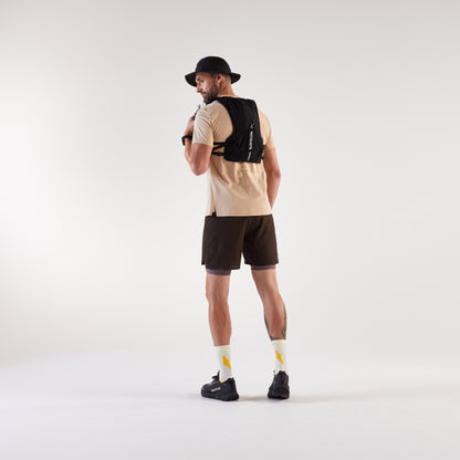 Man wearing a beige shirt, black shorts, and a black backpack on a white background