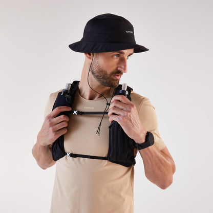 Man wearing a black hat and beige shirt with a black hydration pack on a white background
