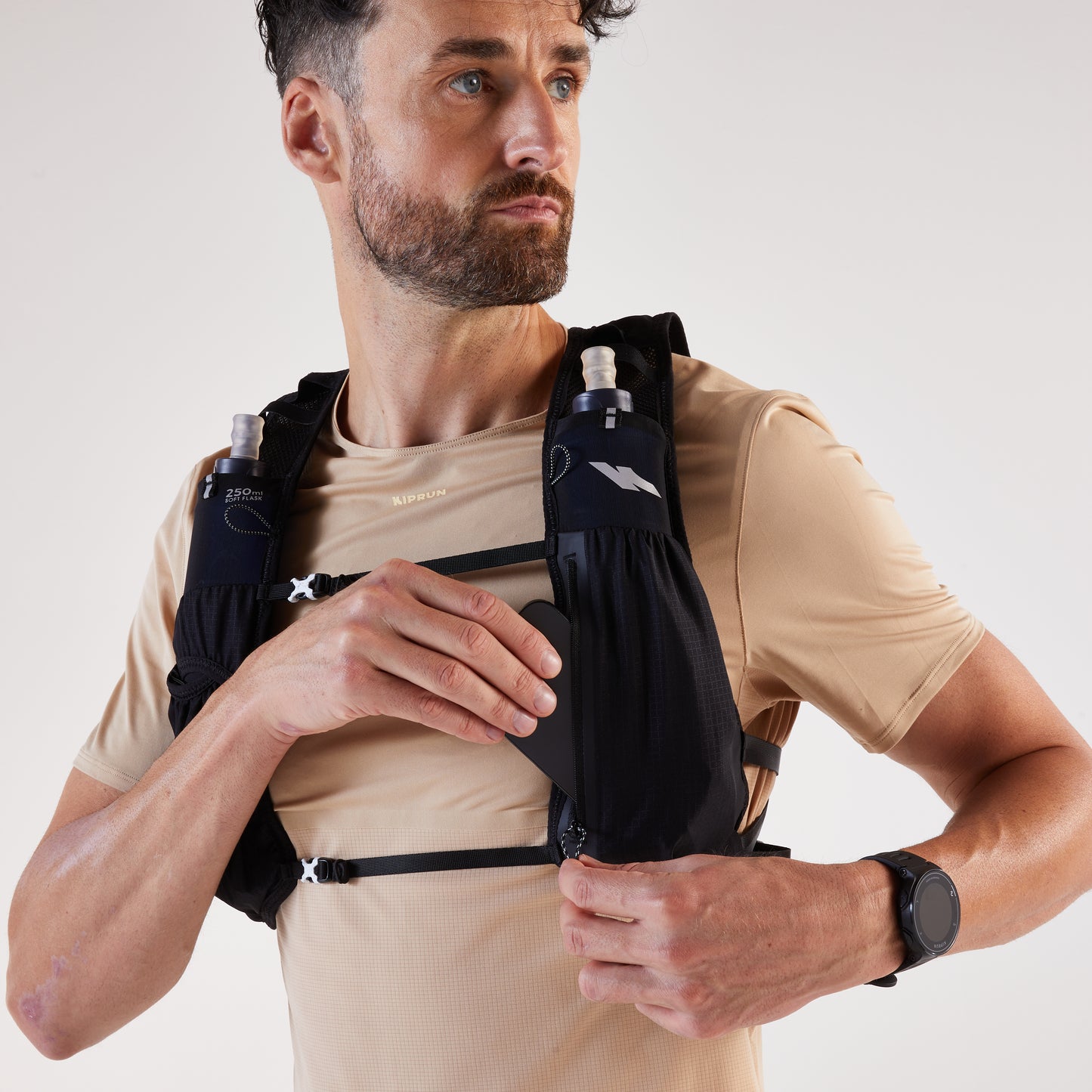 Man wearing a black running vest with hydration bottles on a plain background
