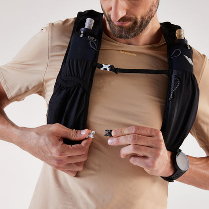 Man wearing a black hydration vest with a beige shirt, holding a small object.