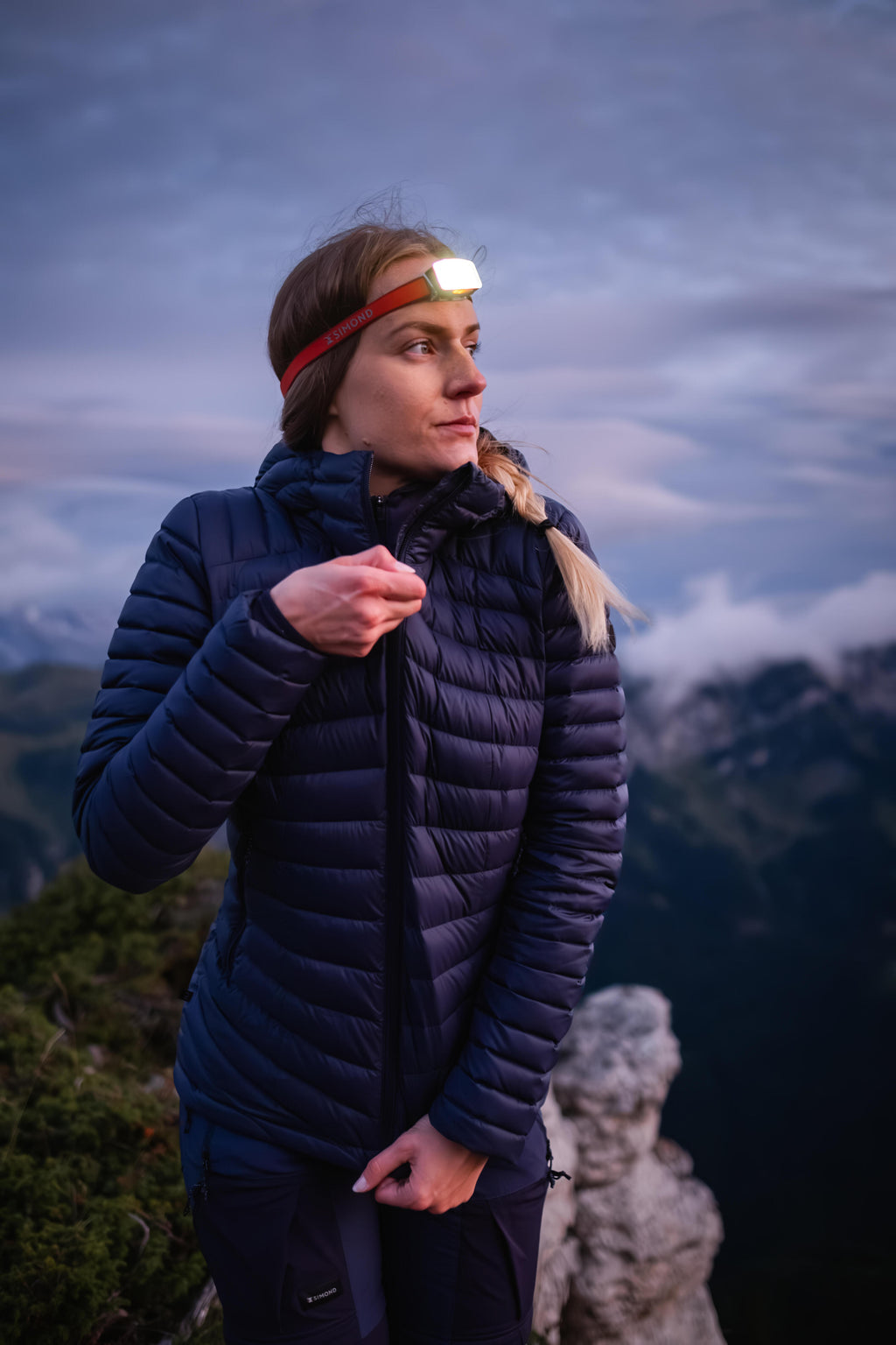 Person wearing a blue puffer jacket with a headlamp on a mountain background