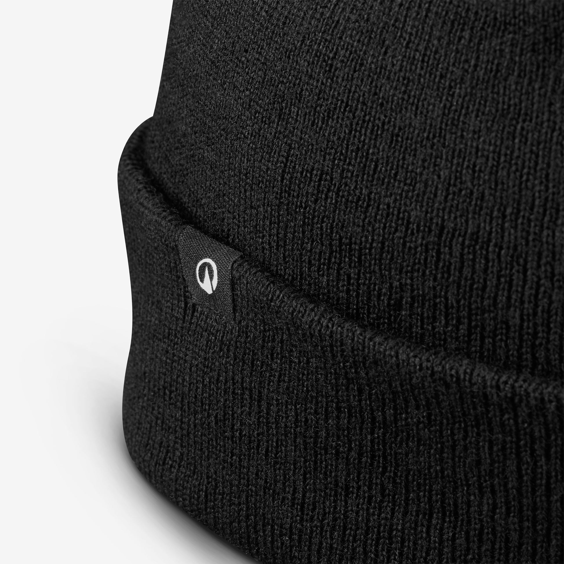 Close-up of a black knit beanie with a brand logo on a light gray background