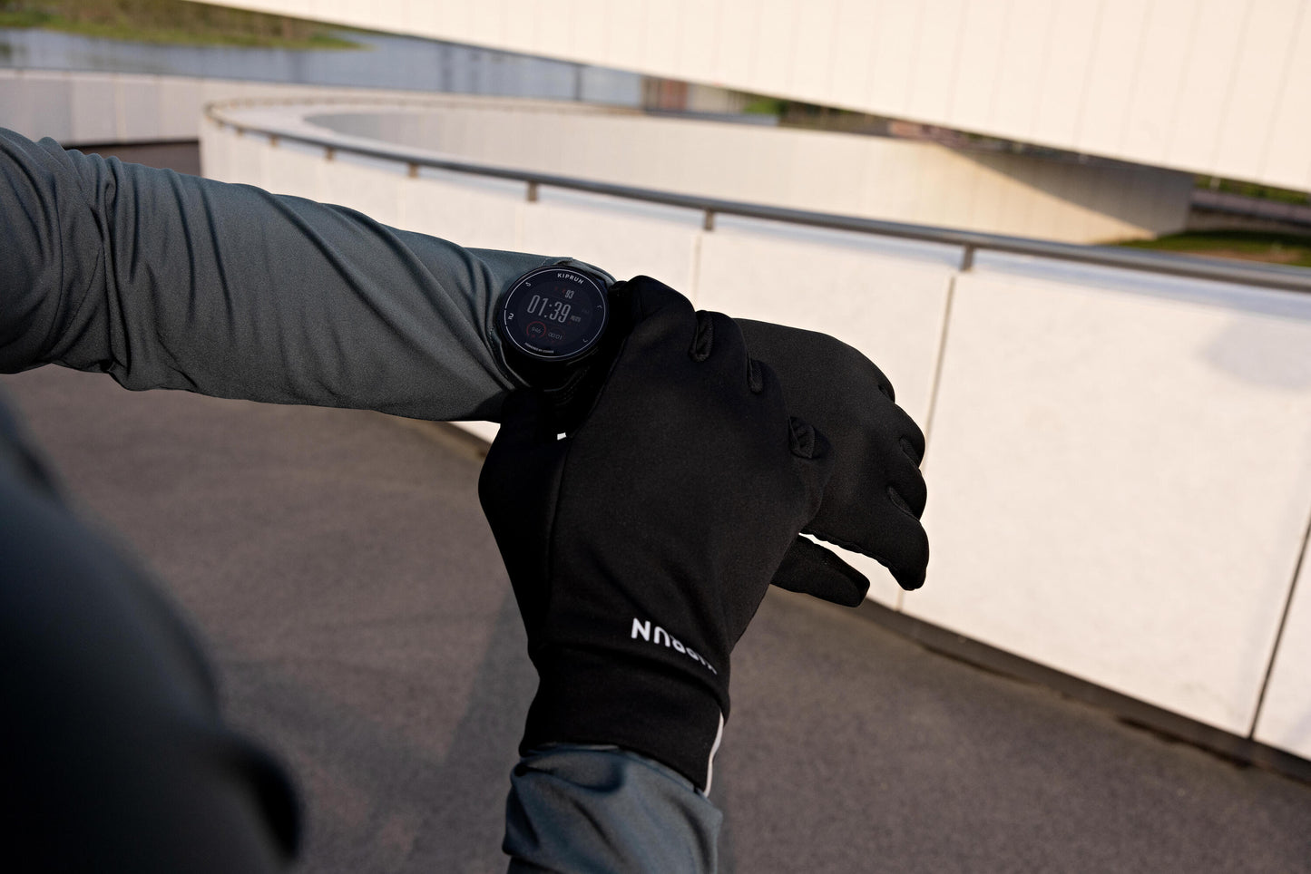 Person wearing black gloves and a gray sleeve, checking a smartwatch on a bridge.