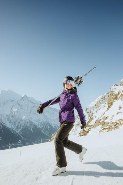 Person in a purple jacket carrying skis on a snowy mountain
